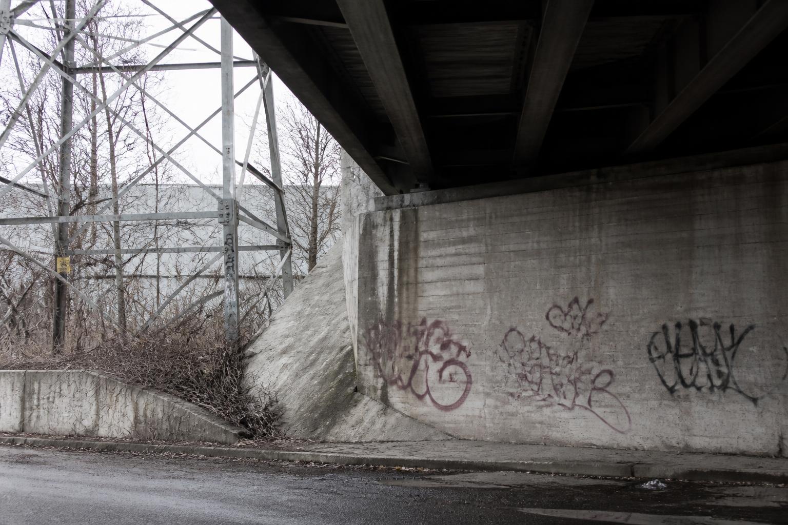 Graffiti markings on concrete infrastructure beneath an urban overpass